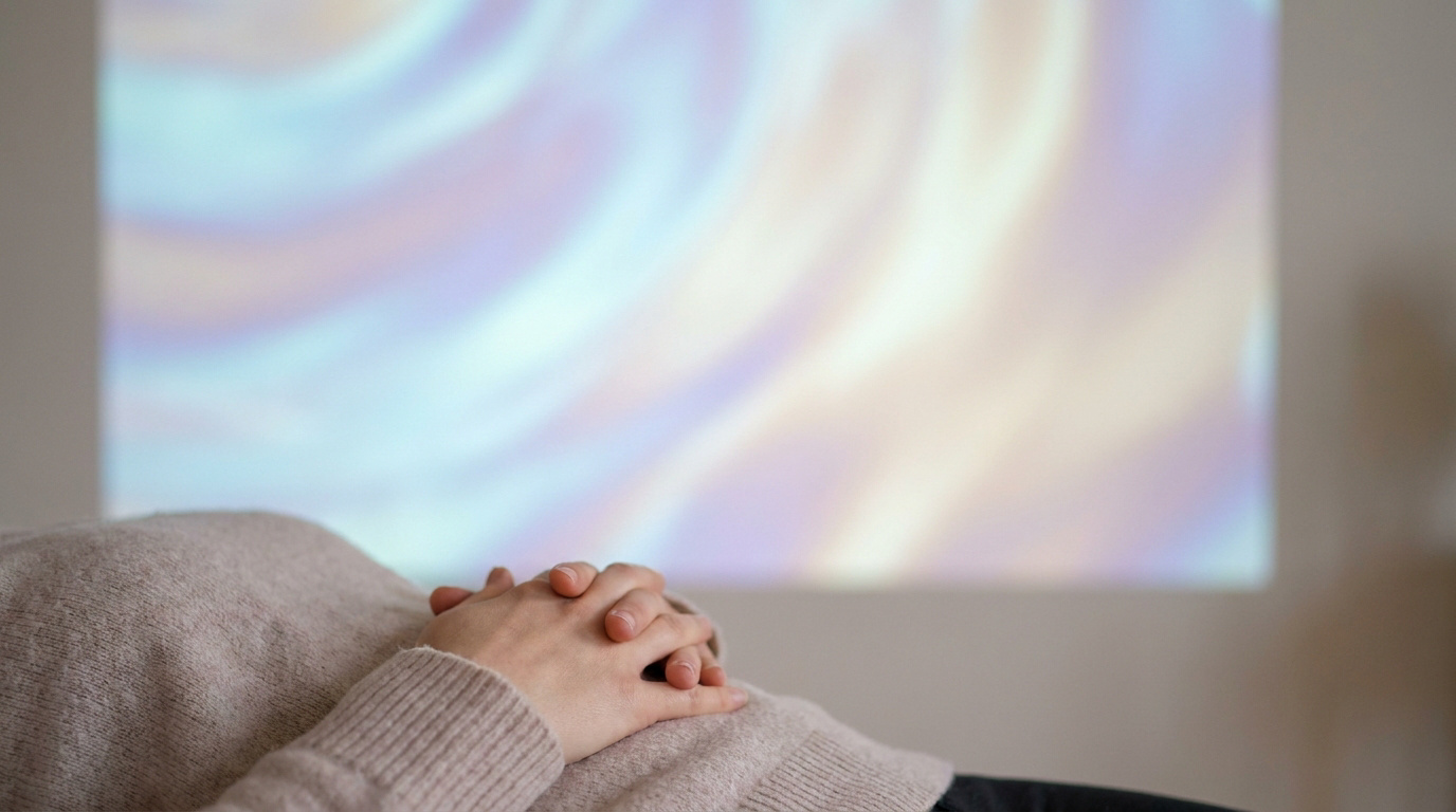 Une personne allongée sur le dos, les mains croisées sur le ventre, face à une projection lumineuse et abstraite.