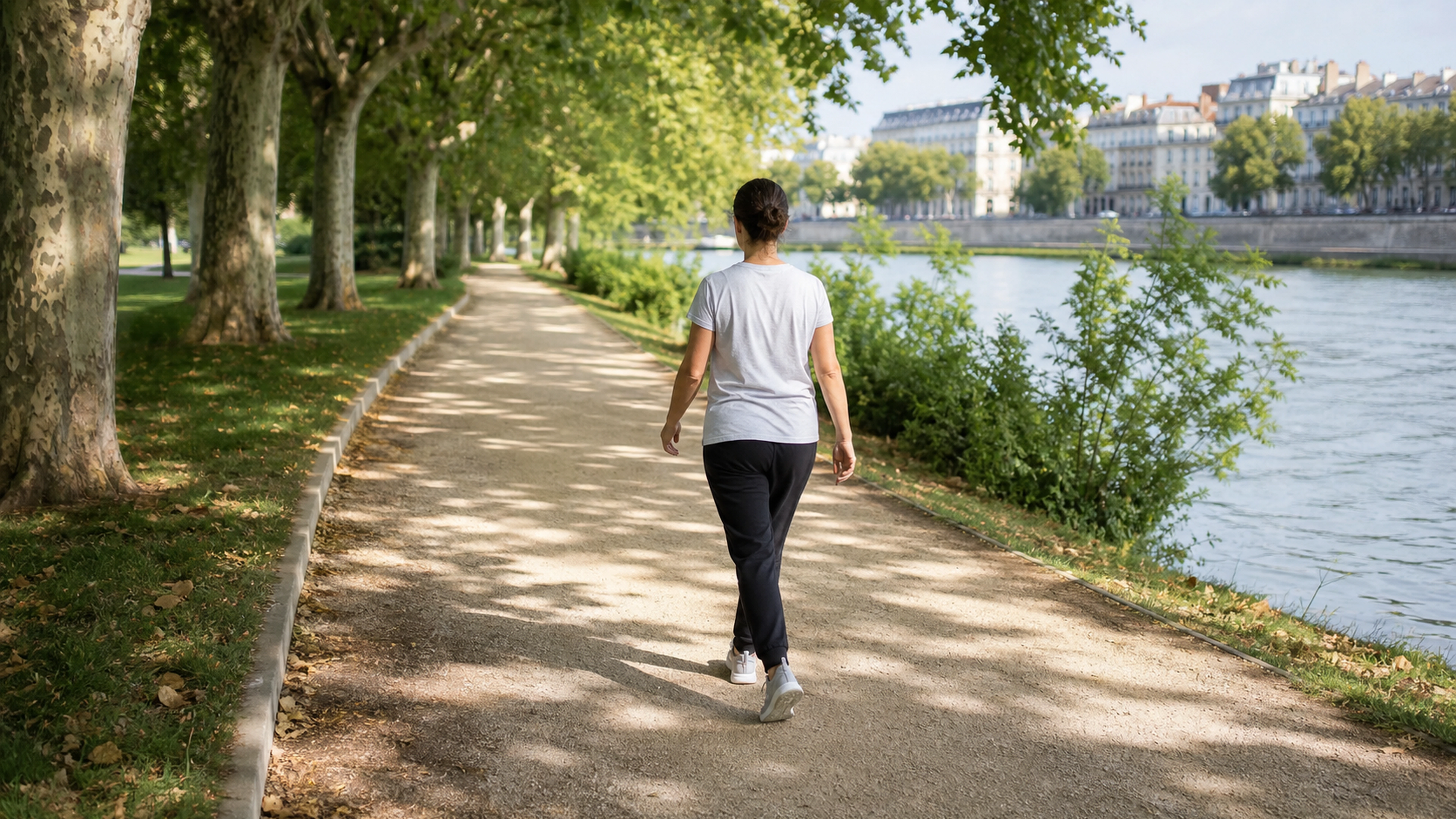 Une femme marche sur un sentier arboré au bord d’une rivière.