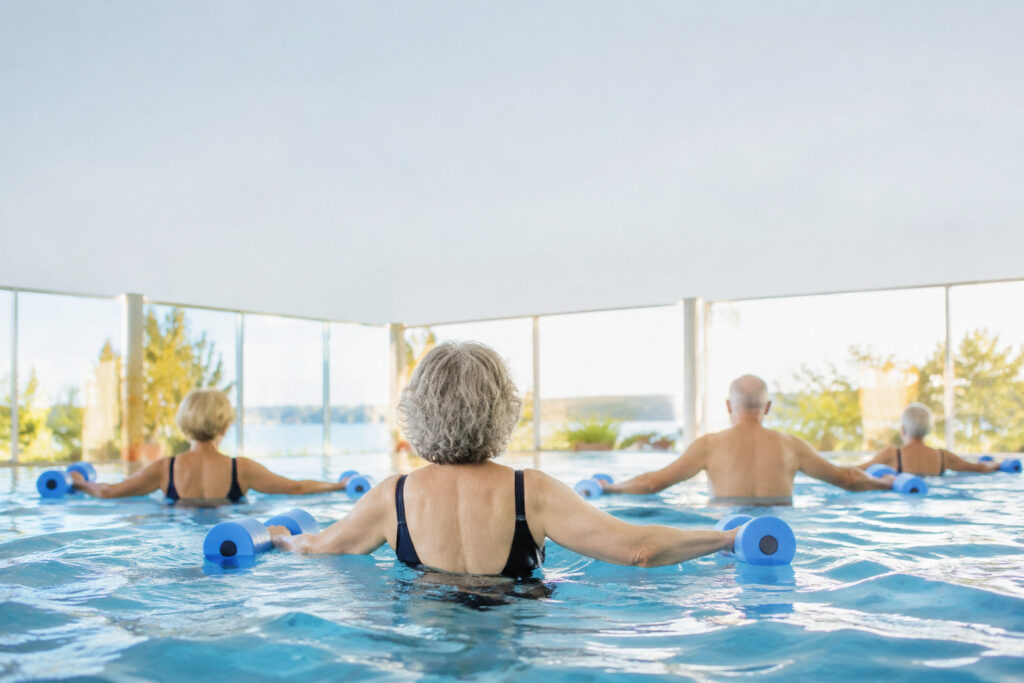 Groupe de seniors faisant des exercices d'aquagym avec des haltères en mousse dans une piscine lumineuse.